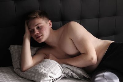 Thoughtful shirtless young man relaxing on bed at home