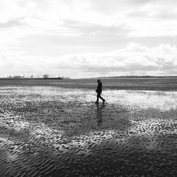 Full length of man walking at wet beach against sky