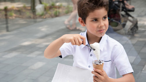Cute child boy with a dirty face eats ice cream, the child enjoys dessert on a walk in the park