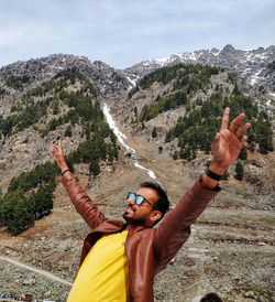 Young man with arms raised standing on mountain against sky