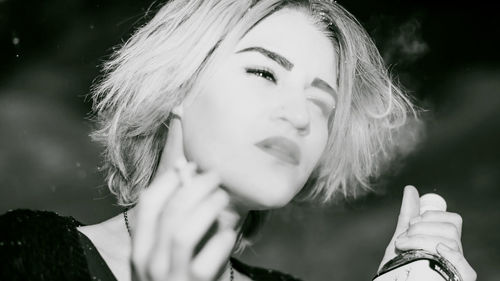 Close-up of young woman smoking cigarette while holding alcohol bottle at night