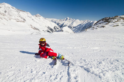 Teenage girl skiing on snow covered land against blue sky