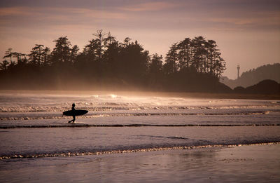 Silhouette surfer walking on calm beach