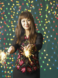 Portrait of smiling young woman with sparklers standing against illuminated lights