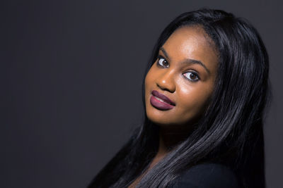 Close-up portrait of smiling young woman against black background