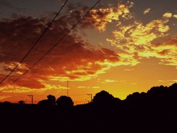 Silhouette electricity pylon against dramatic sky during sunset