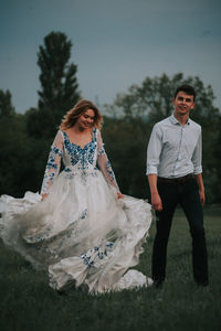 Cheerful couple walking on grass against sky