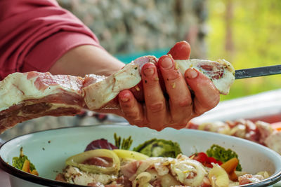 A bowl filled with marinated raw meat and women's hands stringing kebabs on a skewer