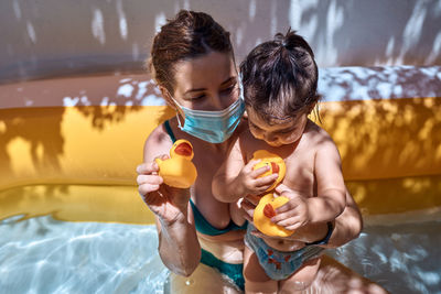 Young mother with a mask in an inflatable pool with her little daughter. safe holiday concept