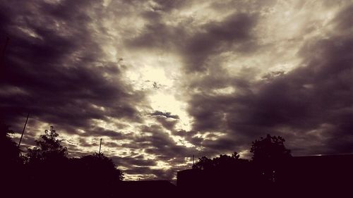 Low angle view of storm clouds over silhouette trees