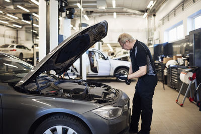 Senior mechanic holding mobile phone examining car at shop