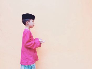 Side view of boy wearing traditional clothing against wall