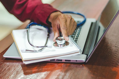 Cropped hands of doctor holding stethoscope on laptop in hospital