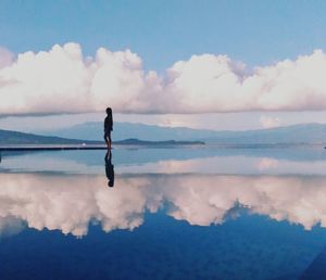 Side view of woman standing by clouds reflection on sea