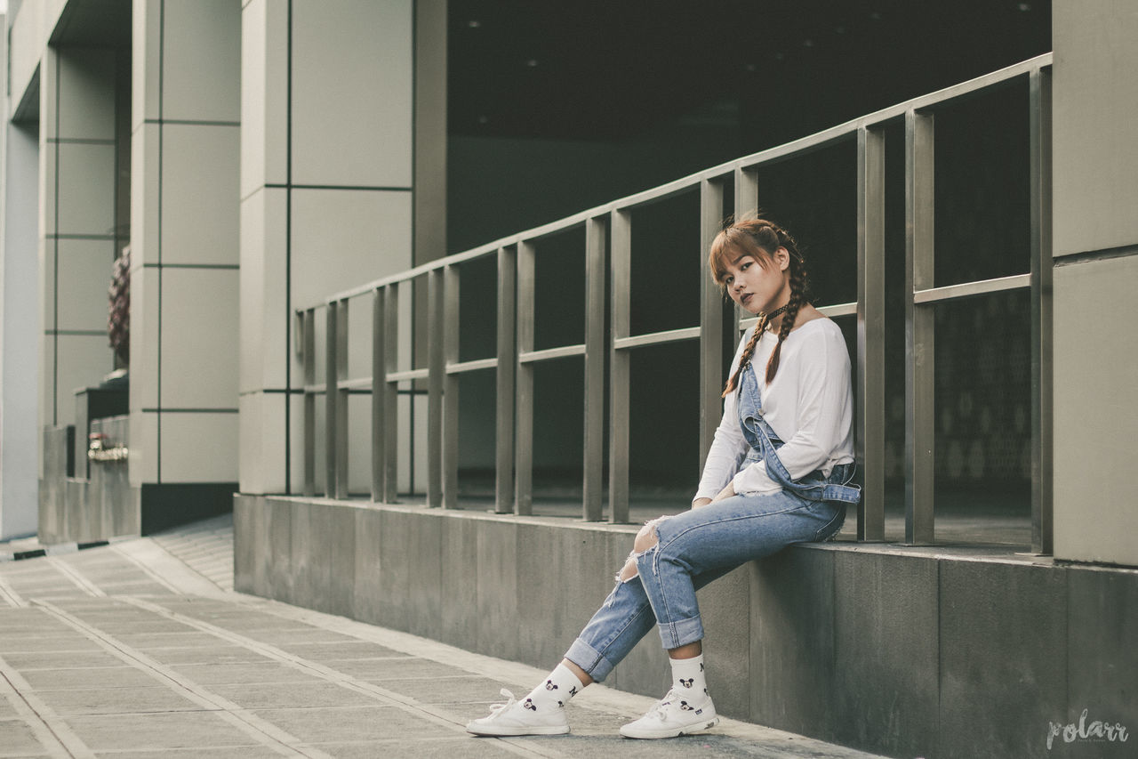 PORTRAIT OF YOUNG WOMAN SITTING ON RAILING