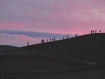 Silhouette people walking on desert at sunset