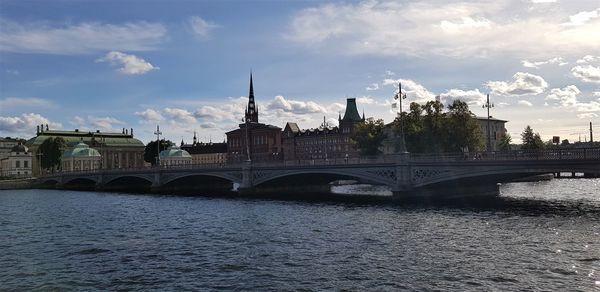 Bridge over river by buildings against sky in city