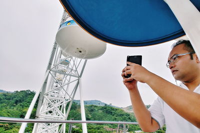 Man using mobile phone against sky