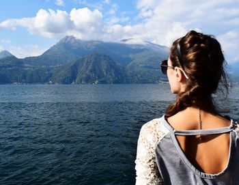 Rear view of woman standing by river against mountains