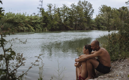Couple in swimsuits hugging by a riverbank during a vacation.