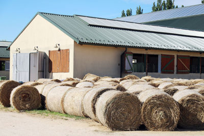 Hay bales on field by building against clear sky