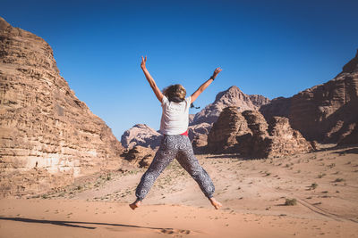 Rear view of woman jumping over field at desert