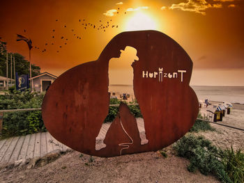 Text on bird by sea against sky during sunset