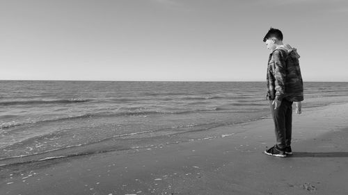 Side view of boy standing at beach against clear sky