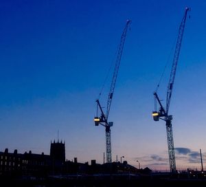 Silhouette cranes at construction site against sky during sunset