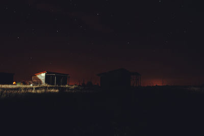 Silhouette buildings on field against sky at night