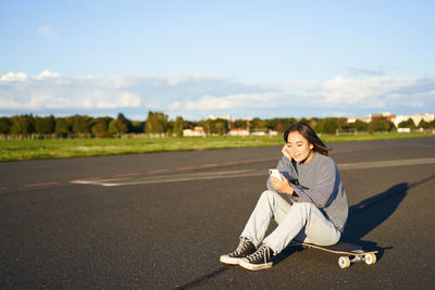 Portrait of young woman sitting on road against sky