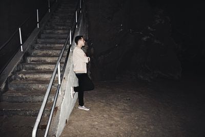 Side view of young man leaning on stairs at night