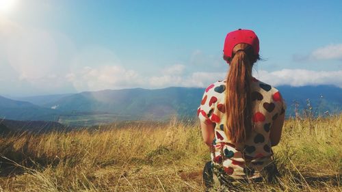 Rear view of young woman sitting on grass field against sky