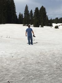 Rear view of man holding camera while standing on snow covered landscape