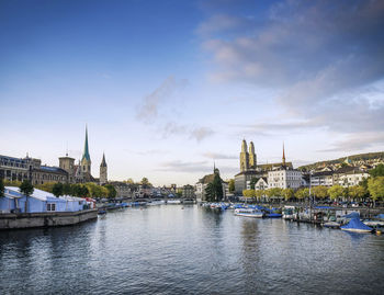 Boats in river by buildings against sky in city