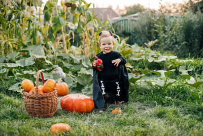 A kid in a carnival devil costume with pumpkins in the garden. halloween costume, tradition