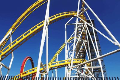 Low angle view of roller coaster against clear blue sky