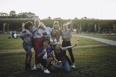 Portrait of happy friends with rainbow flag enjoying at park during sunset