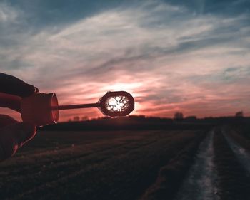 Person holding umbrella on field against sky during sunset