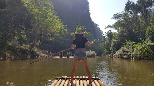 Rear view of woman standing on wooden raft in lake