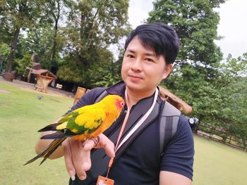 Portrait of young man holding bird on tree