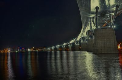 Illuminated bridge over river against sky at night