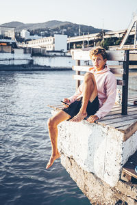 Young man holding mobile phone while sitting at pier