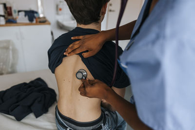 Female healthcare worker examining boy's back with stethoscope in examination room