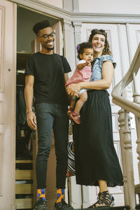 Happy mother and father with daughter at entrance in apartment