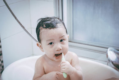 Portrait of cute baby boy brushing teeth in bathtub
