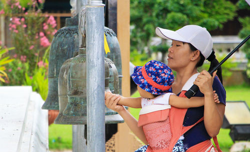Asian woman holding baby ring a bell in a temple on holiday.