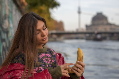 Fashionable young woman holding banana while standing by canal