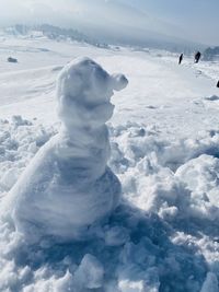 Snowman and people on snowcapped mountain against sky