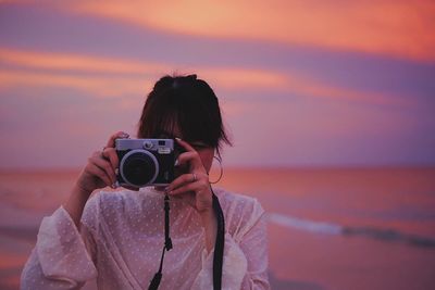 Man photographing with camera on beach against sky during sunset